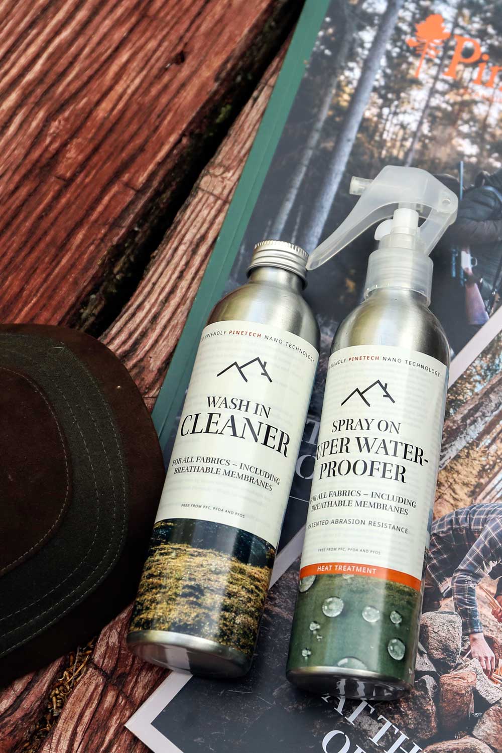 Two metal spray bottles of outdoor waterproofing products labeled 'Wash in Cleaner' and 'Spray on Water-Proof' placed on top of a magazine over a rustic wooden surface.